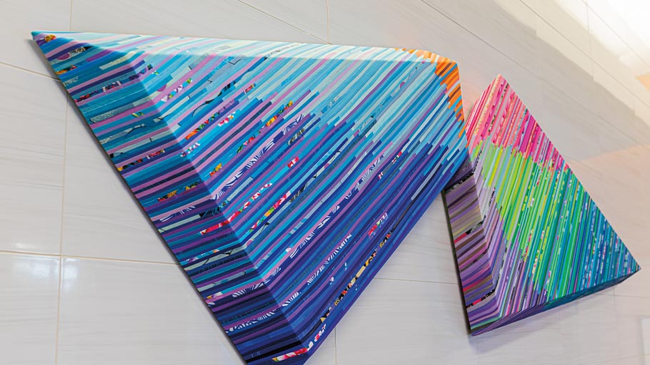 Two three-dimensional art pieces with colorful stripes hang in a Clements University hallway