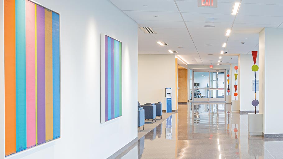A hallway at Clements University Hospital with two framed pieces with colorful vertical stripes and pieces with circles and triangles coming from stone stands