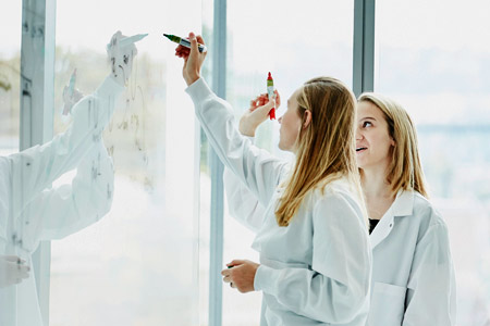 Two female physicians jotting notes on a wall panel