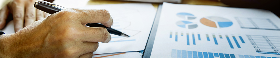 closeup of man's arm and hand holding pen over charts and graphs on table