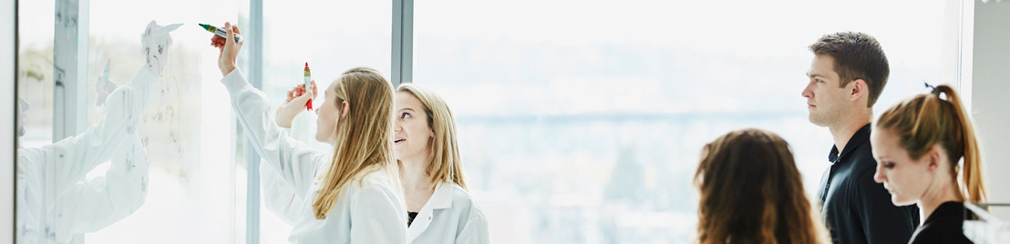 Two female physicians jotting notes on a wall panel while others look on