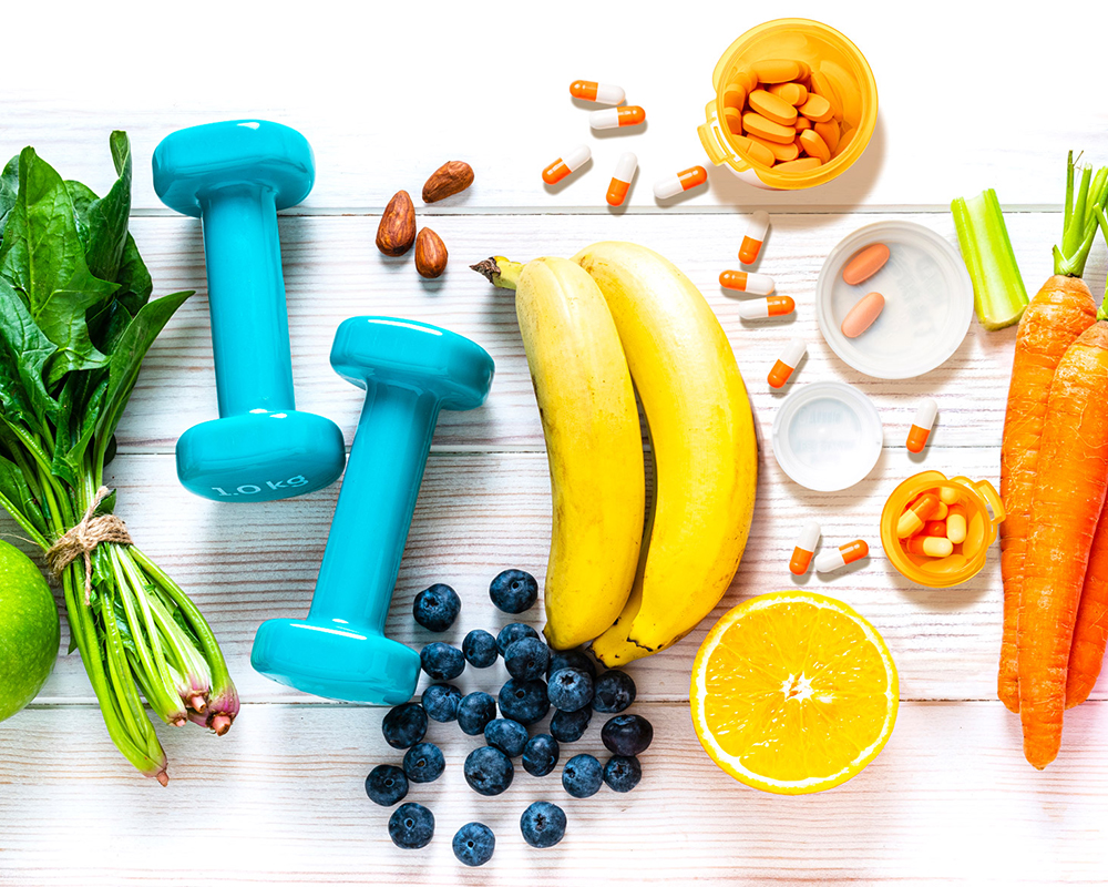 collage of fruits, vegetables, almonds, hand weights, and supplements scattered about atop a wooden surface