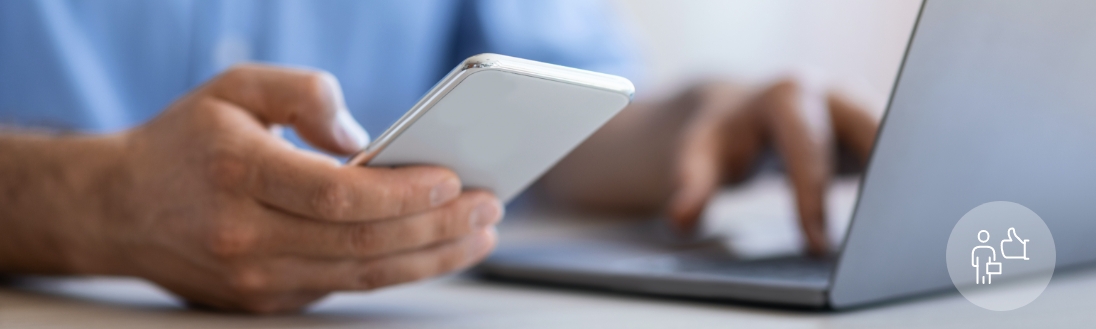 A man holds a cell phone in his right hand while his left hand is on a laptop keyboard