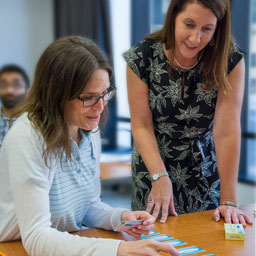 A woman sitting at a desk talks with a woman who stands to her left