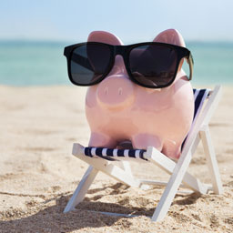 A pink piggy bank wears sun glasses and sits in a beach chair at the beach