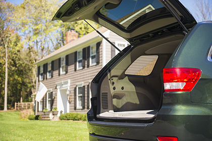 A car with an open trunk sits in front of a house