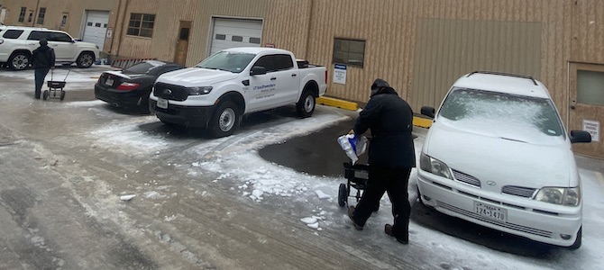 Workers clear ice from around trucks in a UTSW parking lot